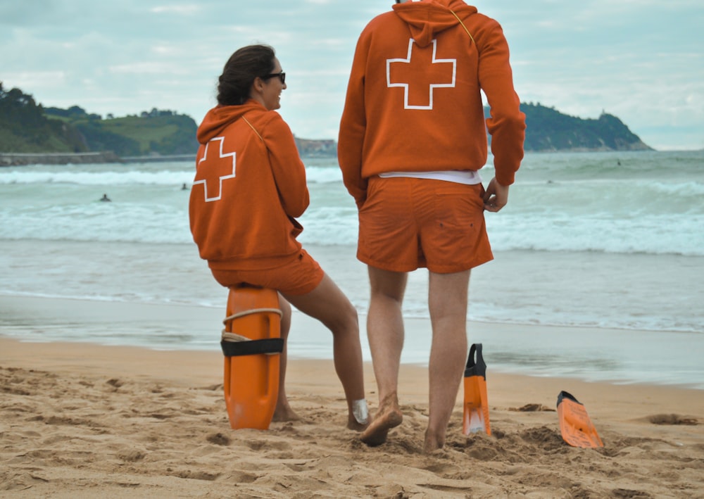 hombre con sudadera con capucha naranja de pie en la playa durante el día