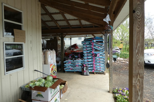 Bags of organic fertilizers stacked in an orderly way inside a regional agricultural store with natural light streaming in.