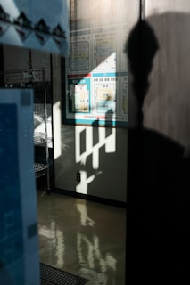 A partial reflection on a polished floor creating an abstract pattern. Wall signage and shelving units are visible in the background, with silhouette of a person partially visible.