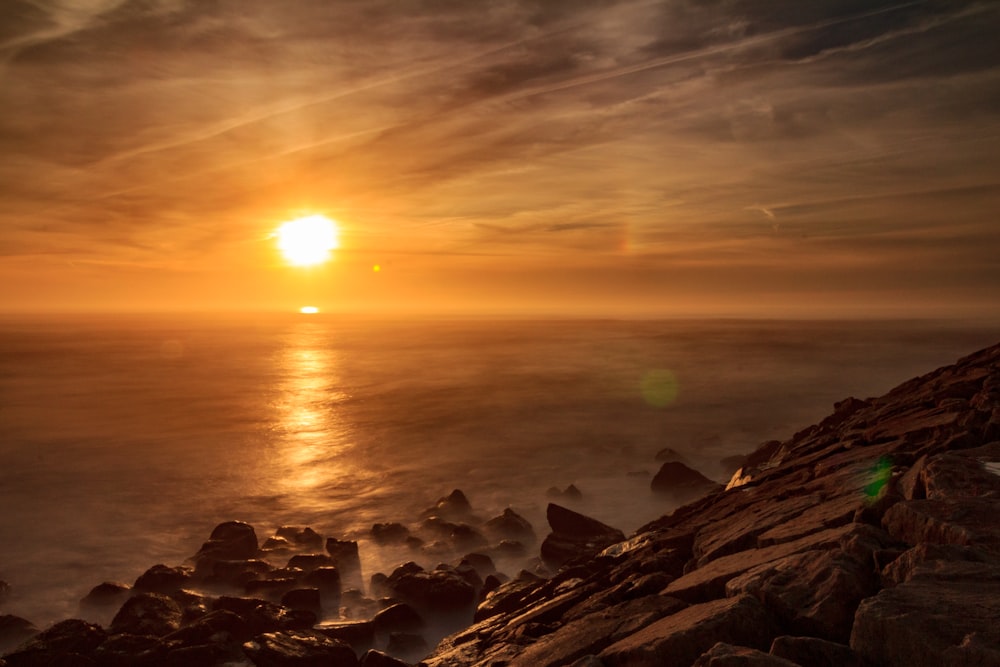 rochas marrons perto do corpo de água durante o pôr do sol