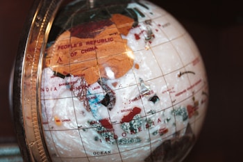A globe made of translucent material displays countries, including China, India, and Indonesia. The surface shows geographical labels with some parts in brown and others in darker and lighter shades. A metallic frame with marked measurements encases the globe.