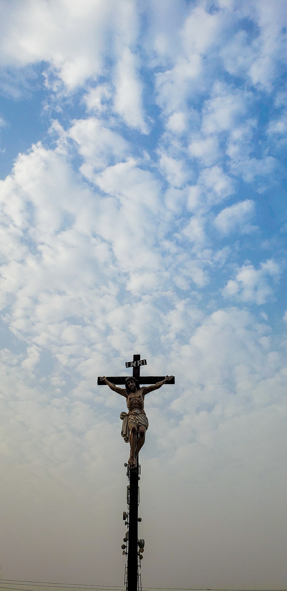 昼間の青空と白い雲の下に茶色の十字架