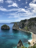 green and brown rock formation beside blue sea under blue and white cloudy sky during daytime
