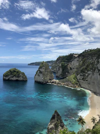 green and brown rock formation beside blue sea under blue and white cloudy sky during daytime