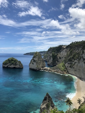 green and brown rock formation beside blue sea under blue and white cloudy sky during daytime