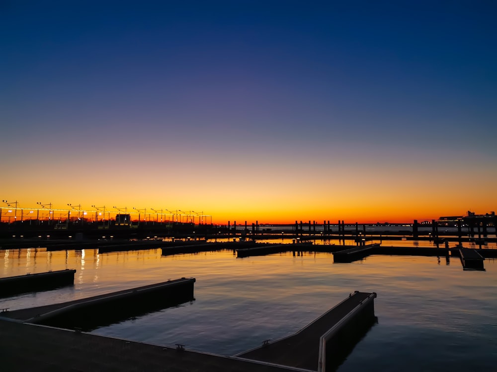 silhouette of dock on body of water during sunset