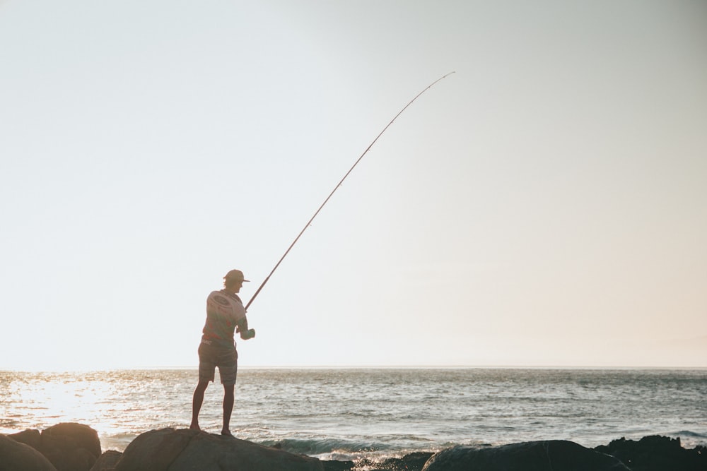 Hombre con camisa blanca y pantalones cortos negros pescando en el mar durante el día
