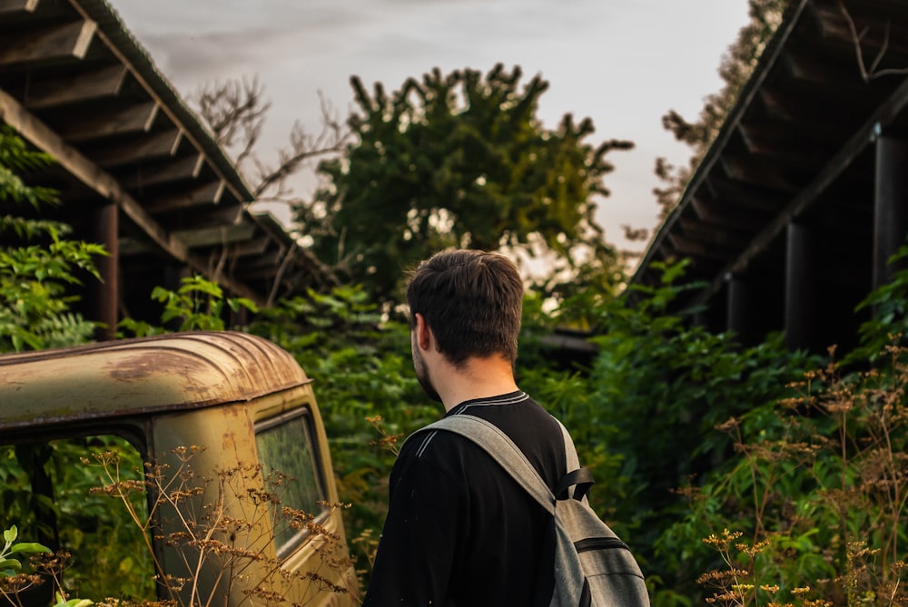 man in black shirt and brown backpack standing near green plants during daytime