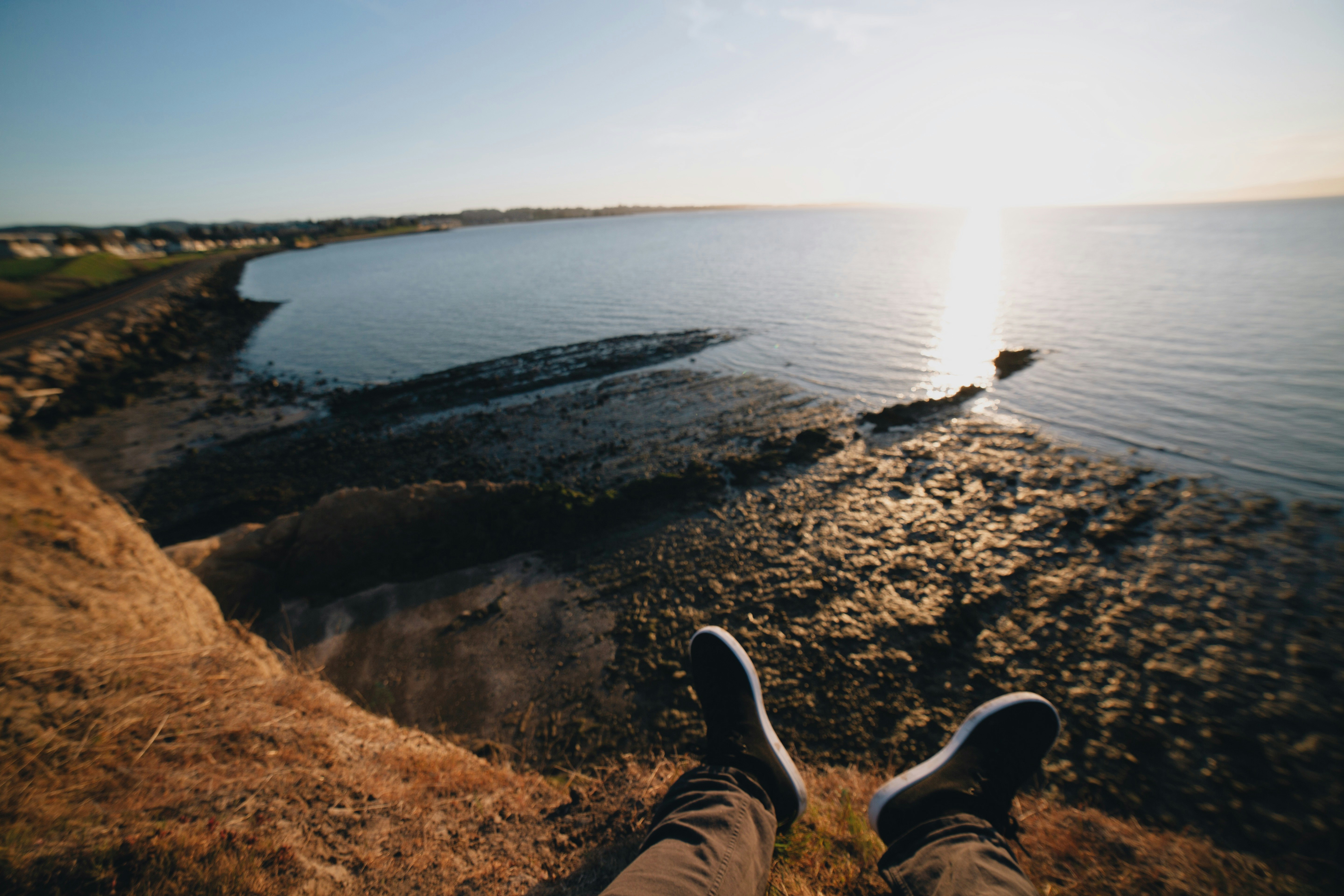 person in black pants and black shoes sitting on brown rock near body of water during