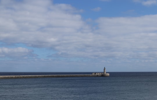 white and brown lighthouse on dock under white clouds and blue sky during daytime in Valletta Malta