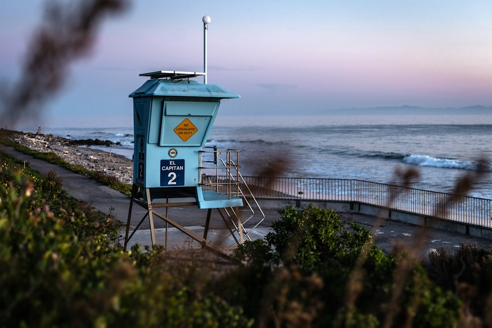 Maison de sauveteur bleu et blanc sur l’herbe verte près de la mer pendant la journée