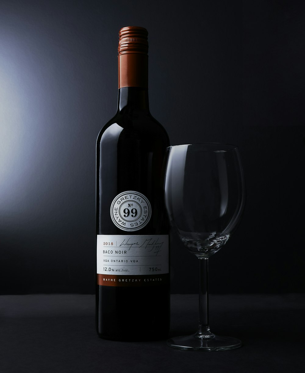 garrafa branca com rótulo ao lado de um copo de vinho transparente