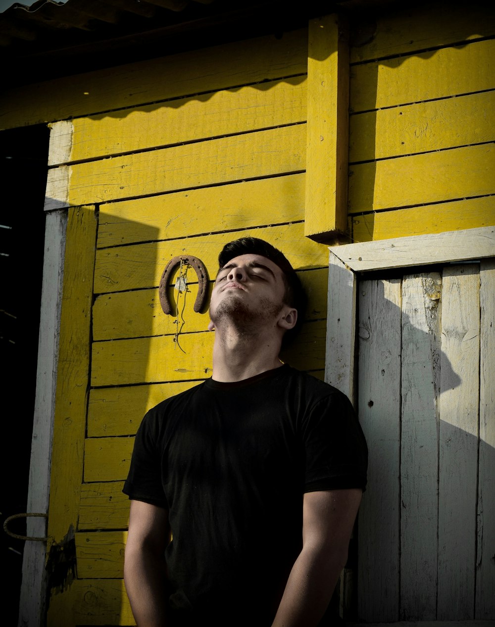 man in black crew neck t-shirt standing beside yellow wooden wall