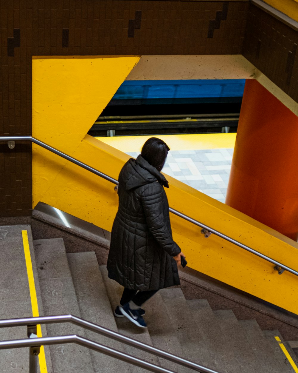 woman in black coat walking on yellow and gray staircase