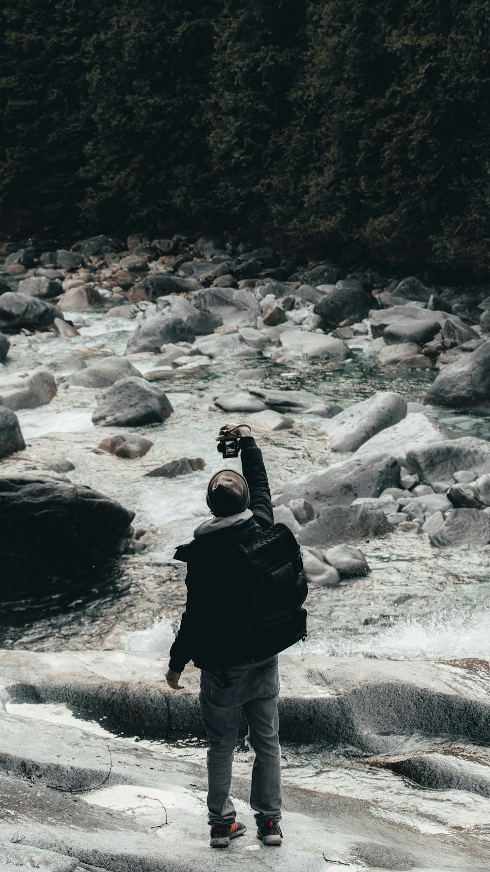 Persona in felpa con cappuccio nera in piedi sul fiume roccioso durante il giorno
