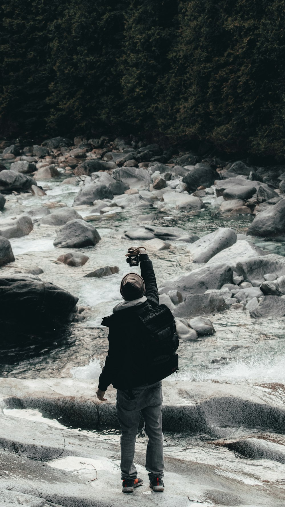 person in black hoodie standing on rocky river during daytime