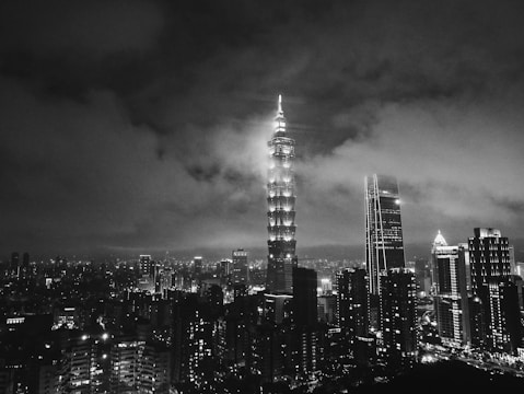 Dramatic low-key photo of a glass skyscraper reflecting golden city lights at night.