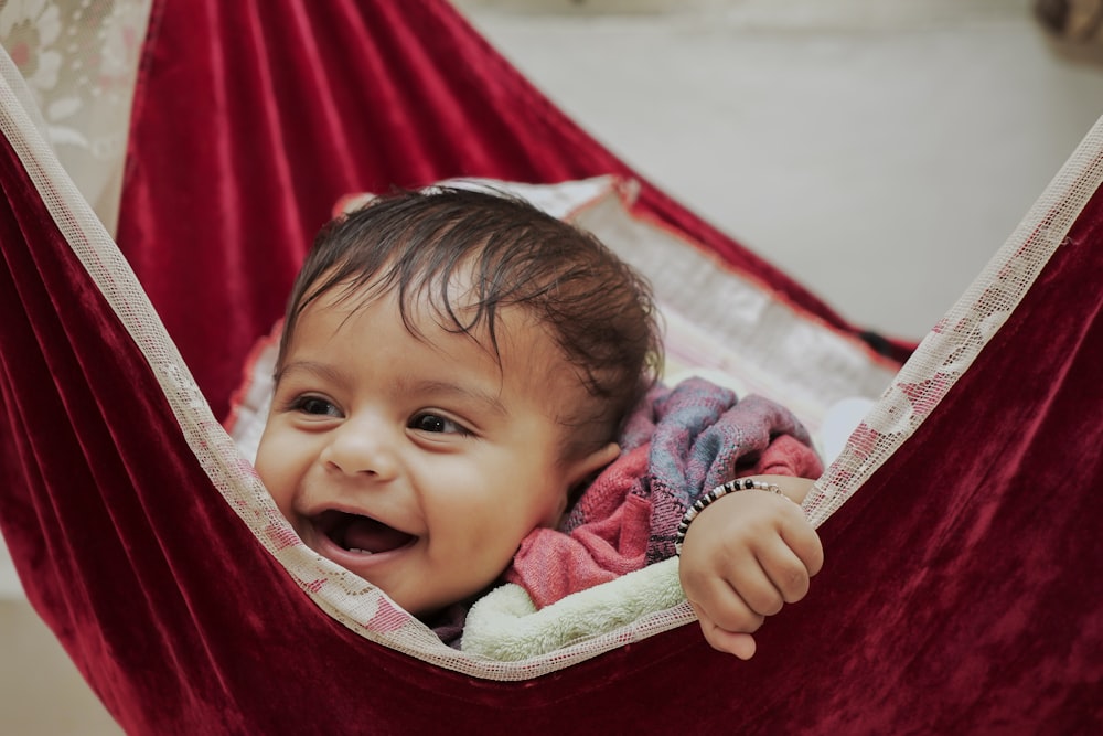 baby in white shirt lying on red hammock