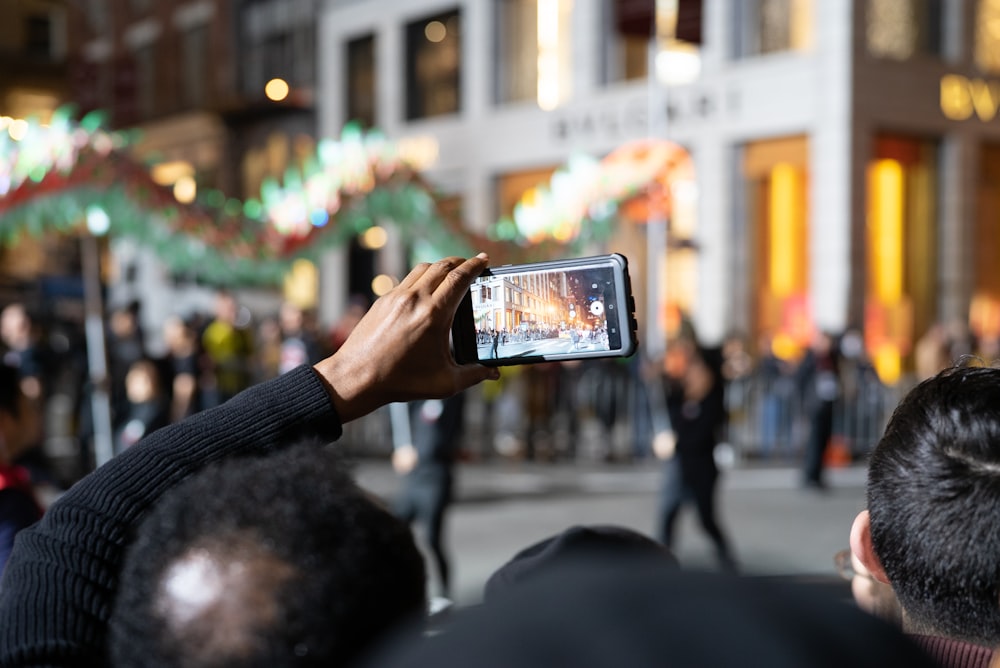 Persona sosteniendo un teléfono inteligente tomando fotos de personas caminando por la calle durante el día