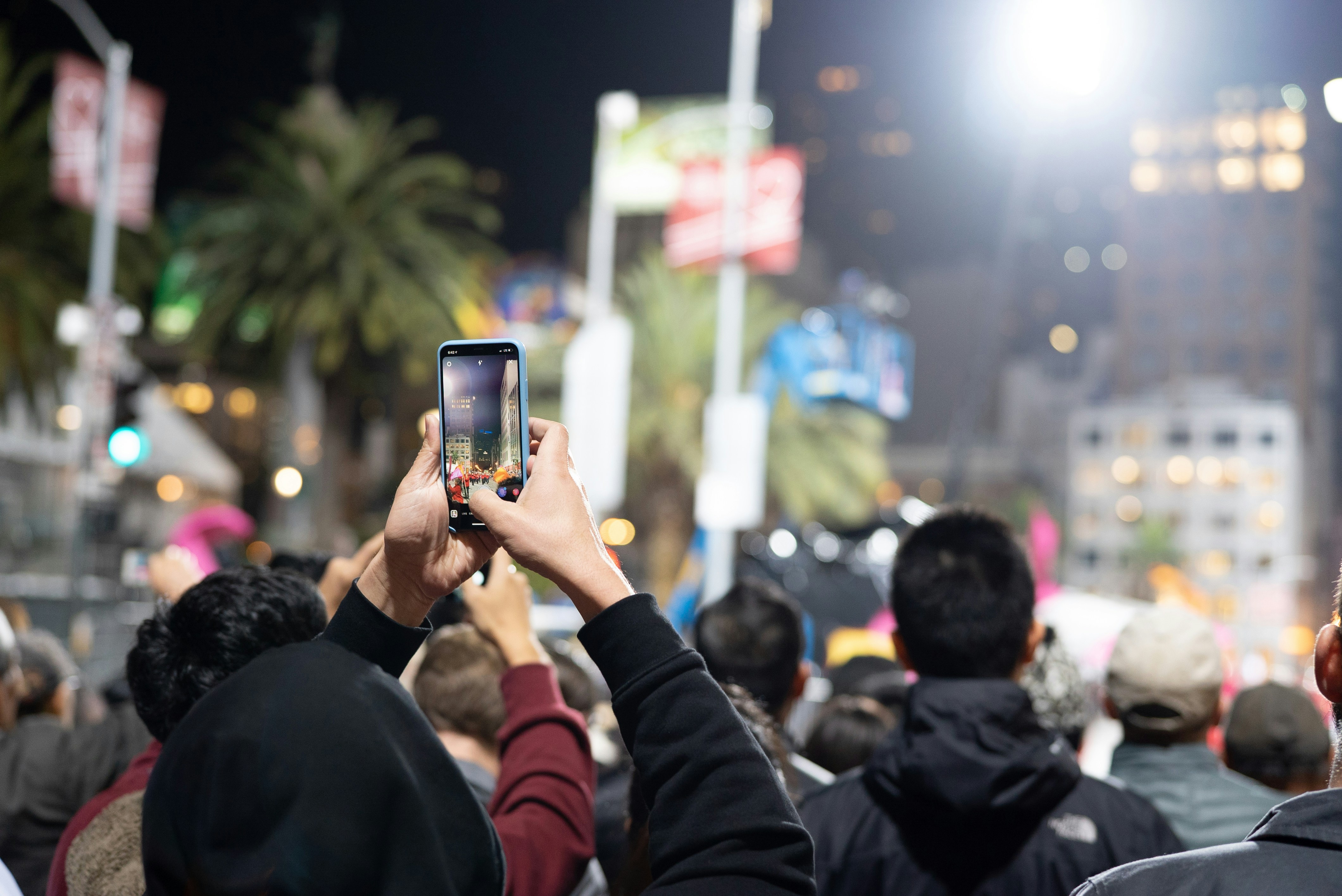 man in red jacket holding iphone taking photo of people during nighttime