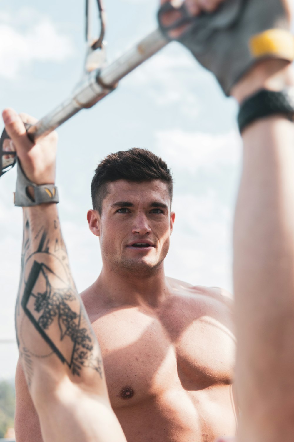 topless man with tattoo on his arm holding a black and silver rod