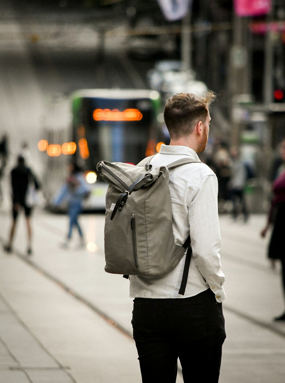 man in white dress shirt and black pants carrying black backpack walking on sidewalk during daytime