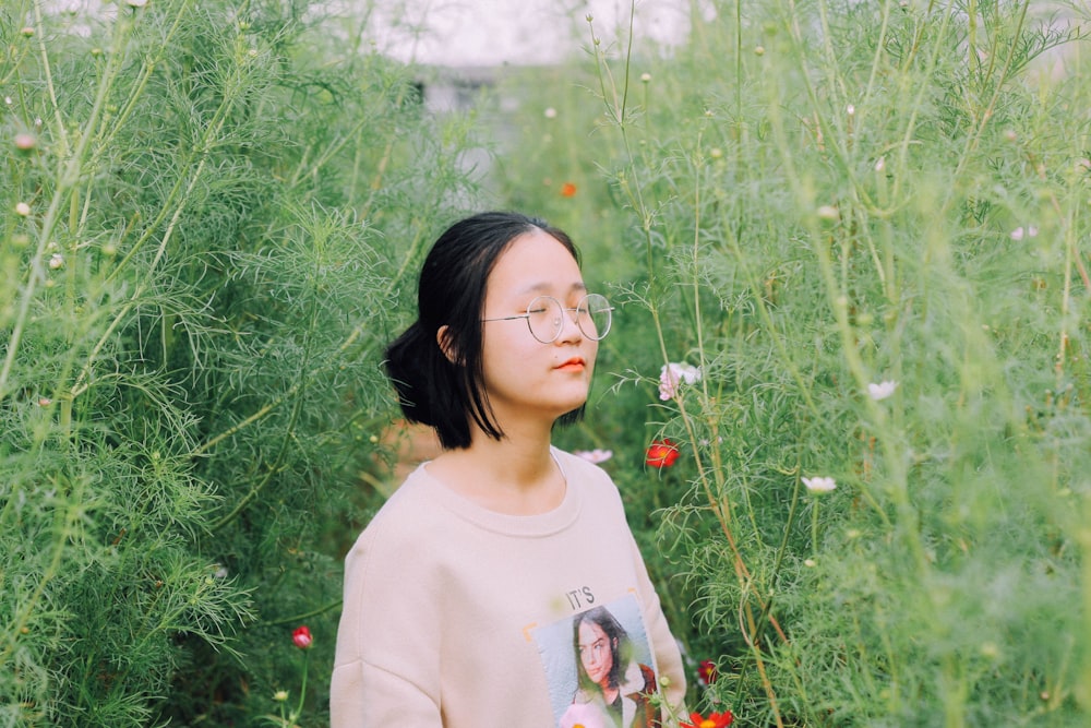 Femme en chemise à manches longues à col rond blanc debout sur le champ d’herbe verte pendant la journée