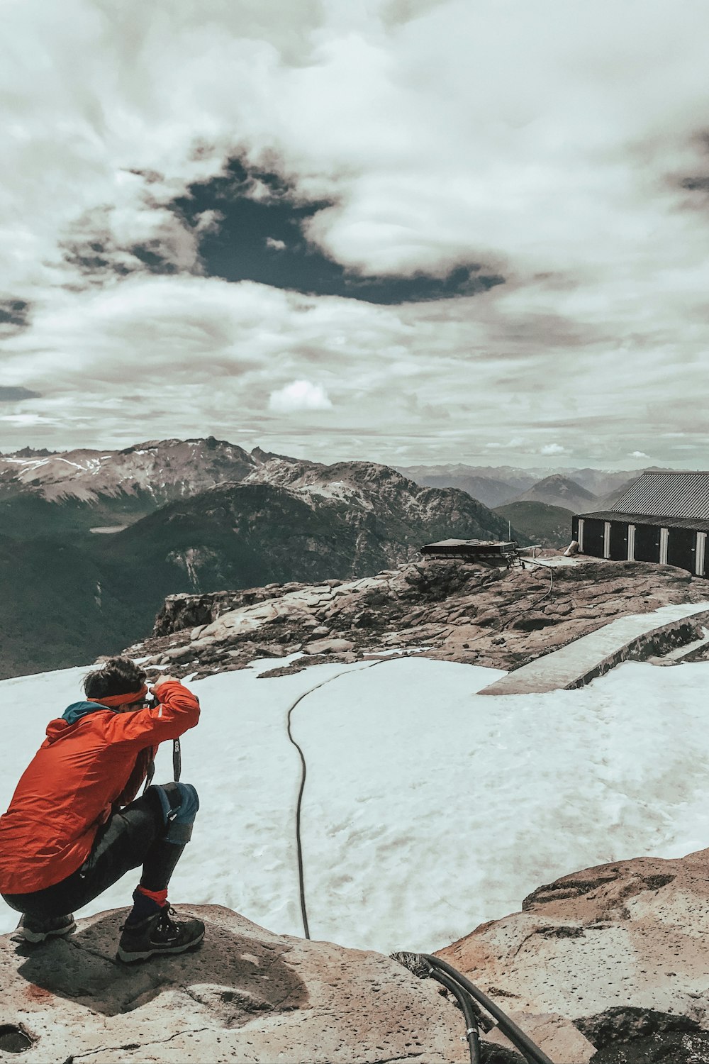 man in orange jacket and black pants sitting on rock