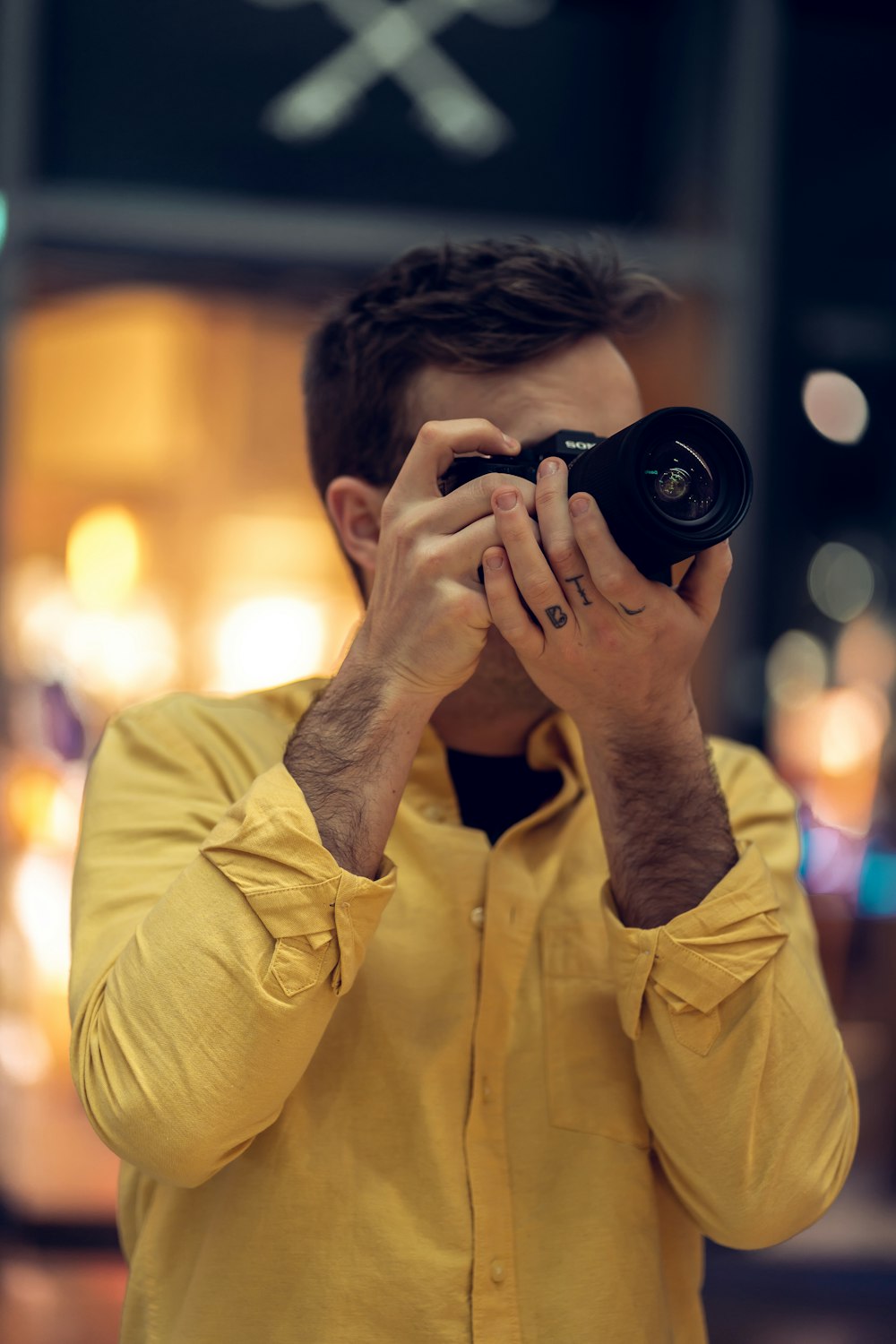 man in yellow dress shirt holding black camera