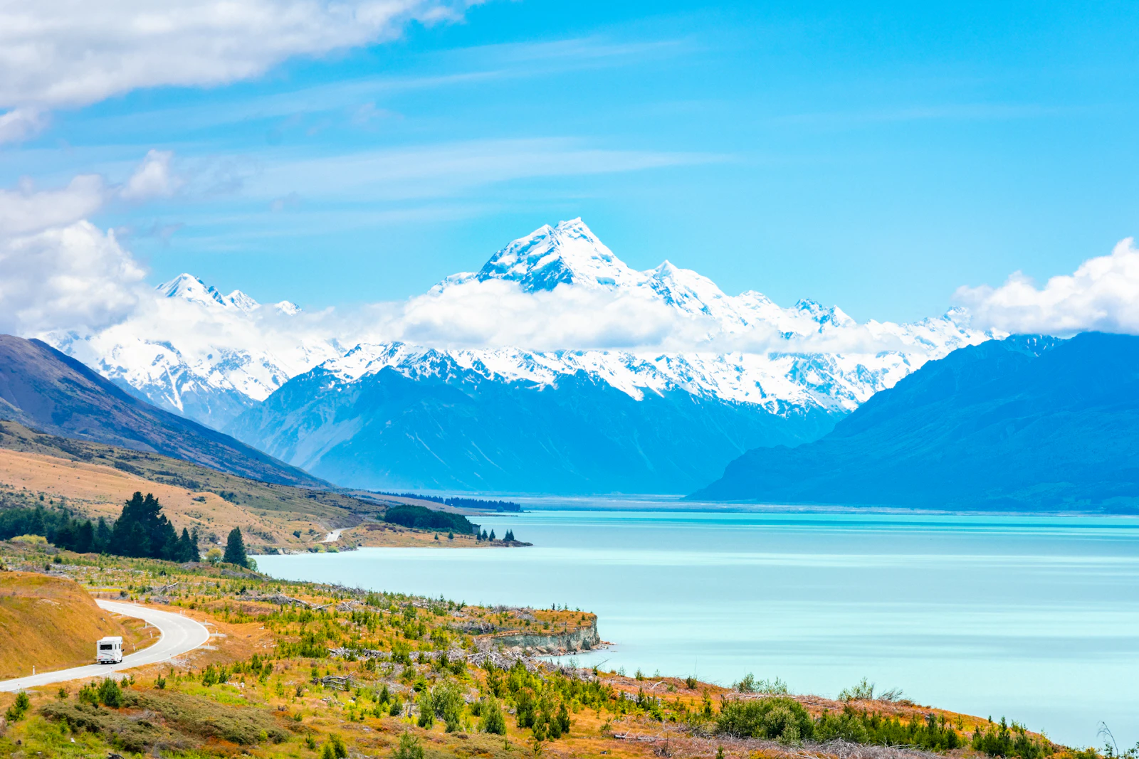 A campervan stands near a lake and mountain road in New Zealand