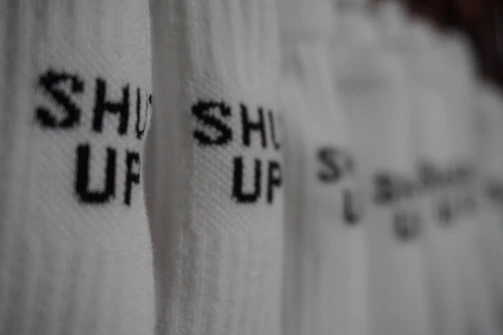 A close-up of a t-shirt with bold, sarcastic office humor typography in muted charcoal on a washed black background.