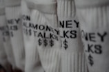 Several pairs of white socks feature the phrase 'MONEY TALKS' along with dollar signs in black text. The focus is on the texture of the fabric and the bold lettering.