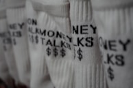Several pairs of white socks feature the phrase 'MONEY TALKS' along with dollar signs in black text. The focus is on the texture of the fabric and the bold lettering.