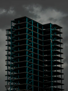 A wide shot of a building framework with red steel beams against a cloudy sky.