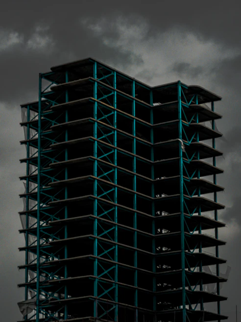 A wide shot of a building framework with red steel beams against a cloudy sky.
