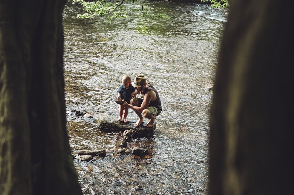 3 women sitting on rock in river during daytime