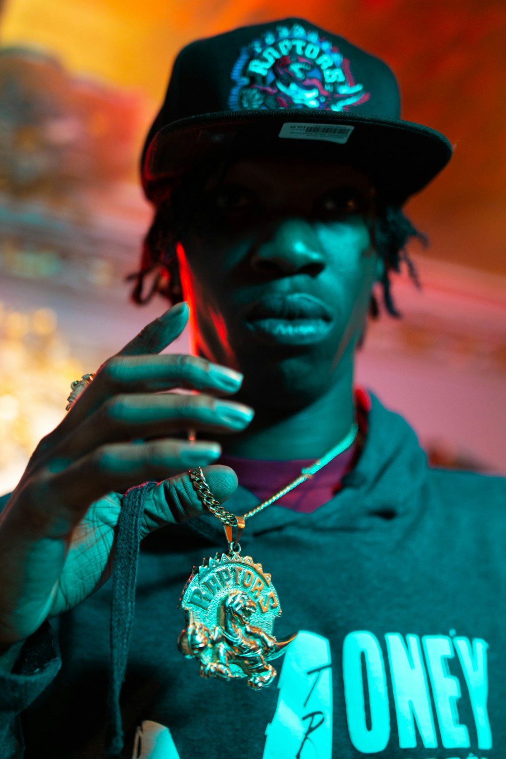 man in grey shirt with gold necklace and black hat