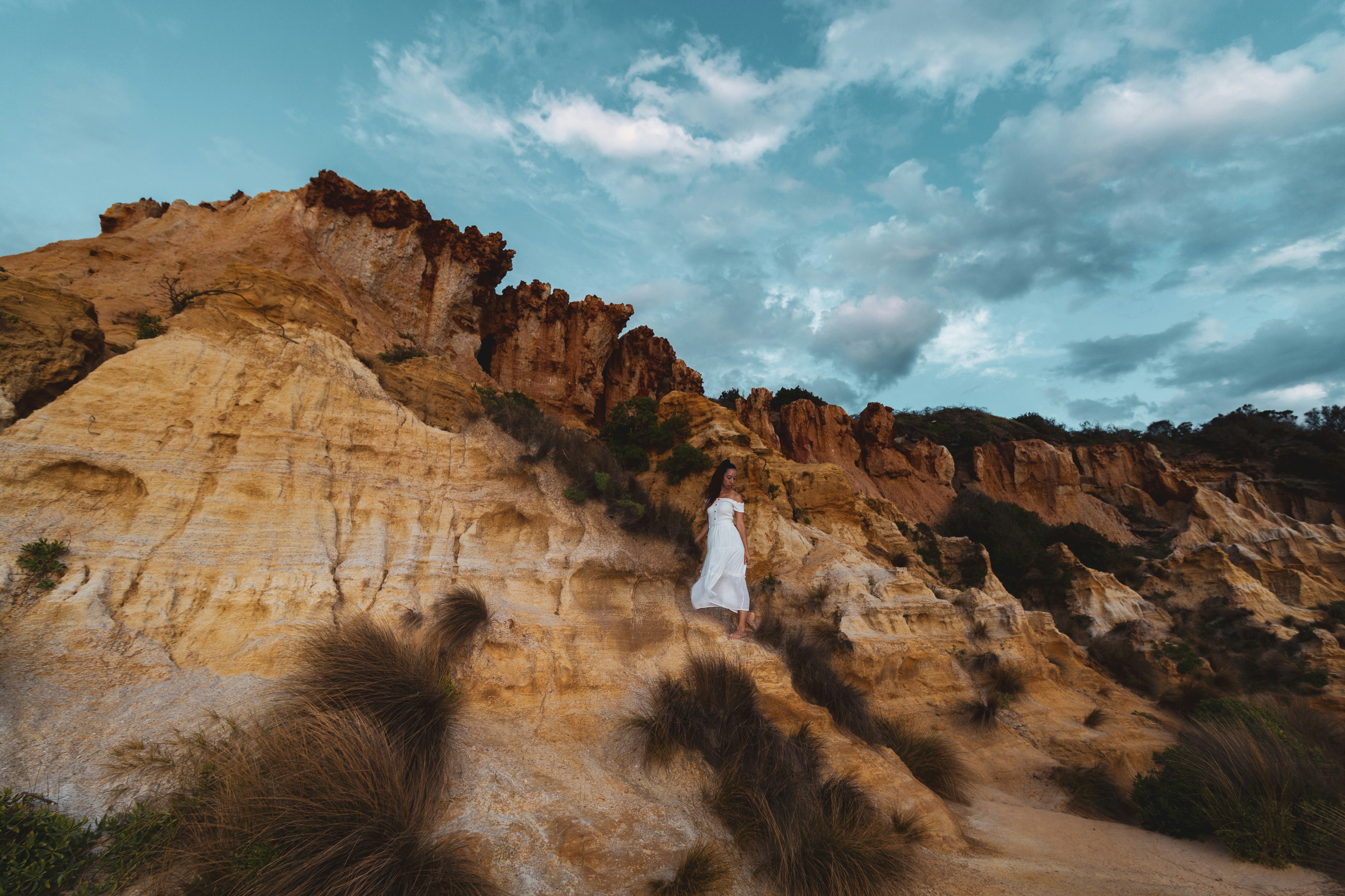 woman in white dress standing on brown rock formation under white clouds and blue sky during