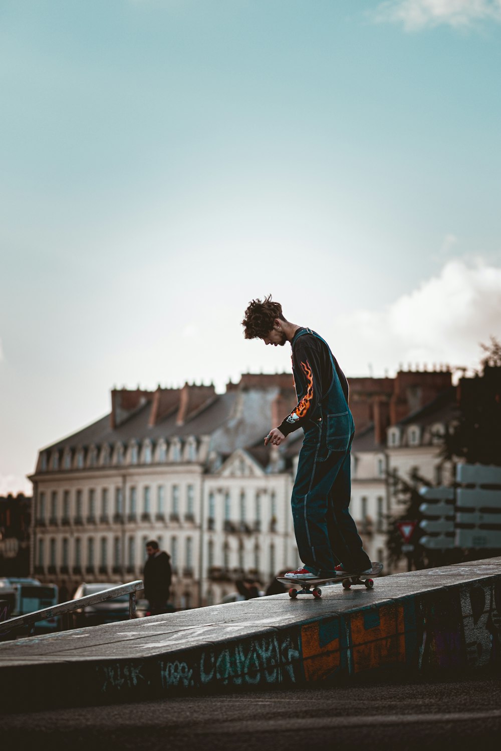 Homme en chemise à manches longues bleue et rouge et pantalon noir debout sur un trottoir en béton gris