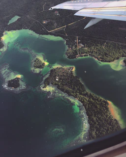 An aerial shot of a plane taking off over a sparkling blue sea coastline.