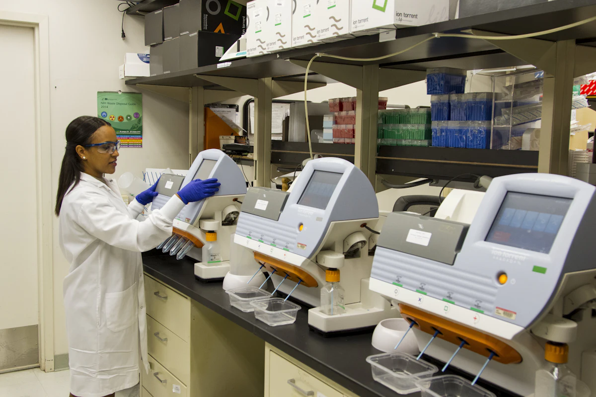 A scientist in protective clothing operating an automated laboratory analyser.