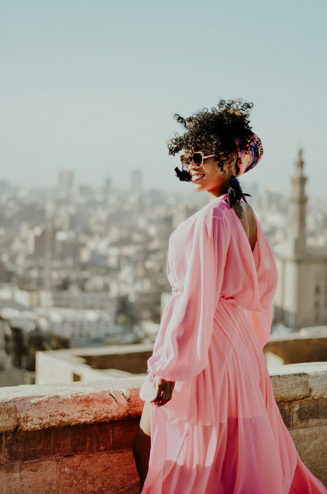 woman in pink dress standing on brown concrete wall during daytime