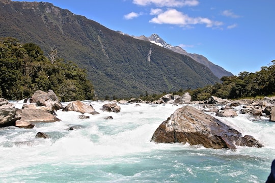 green mountain beside body of water during daytime in Haast New Zealand