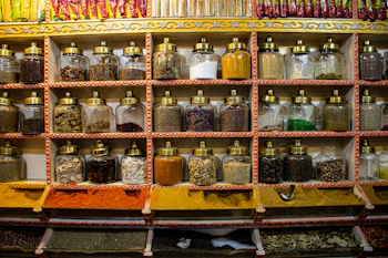 Vibrant jars of colorful homemade masalas arranged on a wooden shelf.