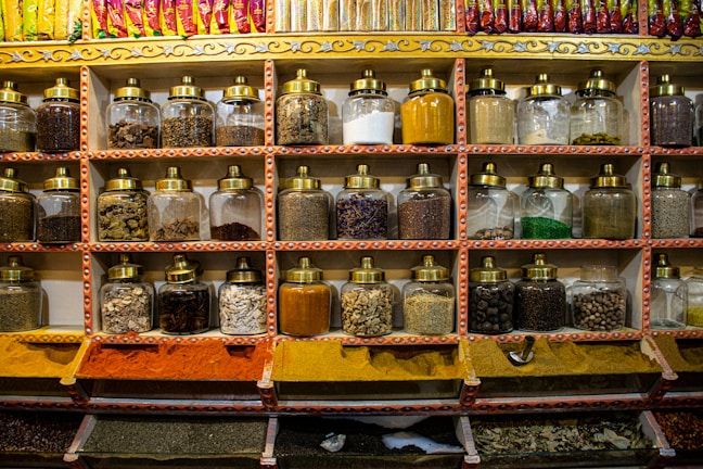 Glass jars filled with different spices lined up on a wooden shelf.