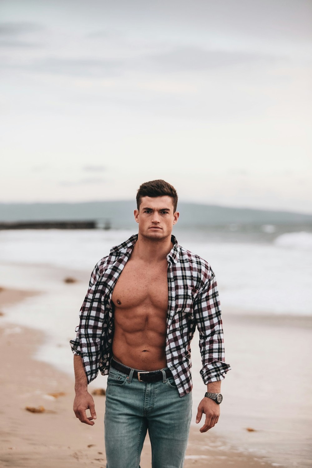 man in black and white plaid dress shirt standing on beach during daytime