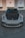 A high-performance sports car is parked in front of a beige industrial building with three white garage doors. The car has a sleek design with a black hood and front grille.