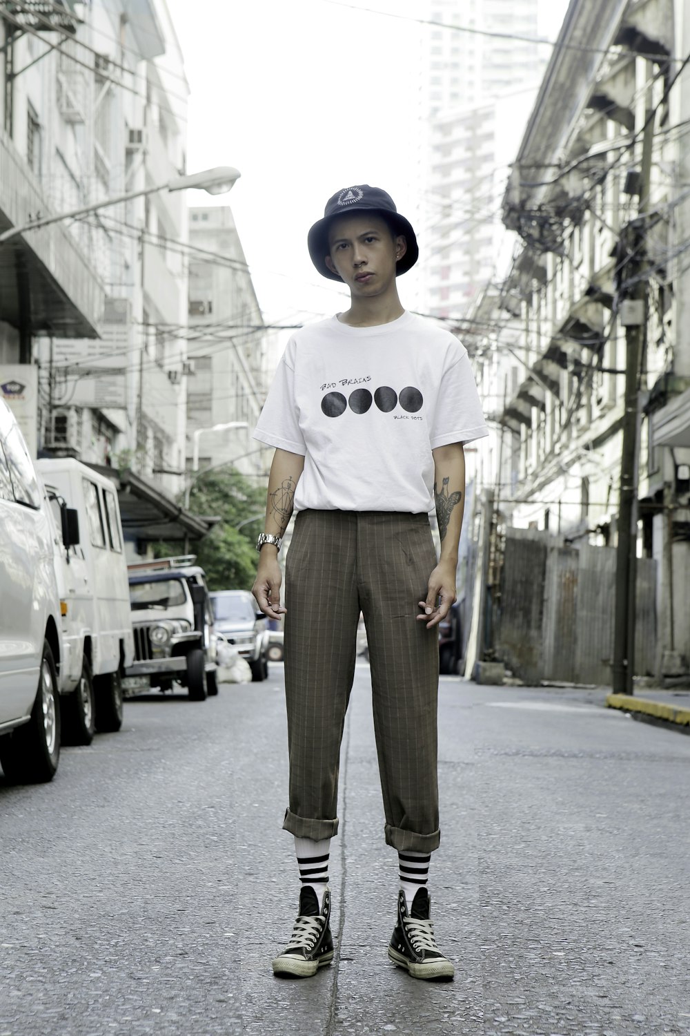 man in white crew neck t-shirt and brown pants standing on road during daytime