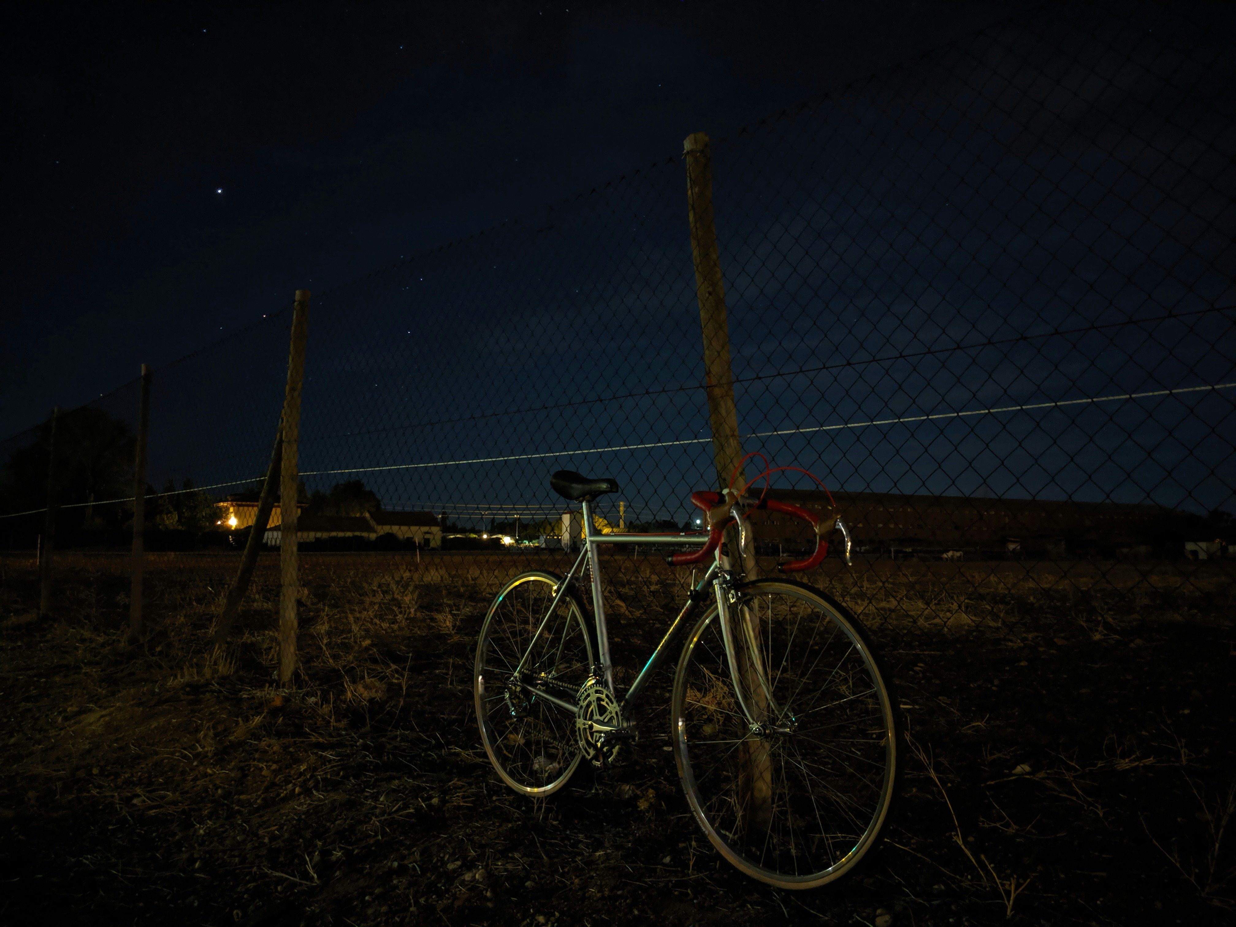 black and white road bike leaning on gray metal fence during night time