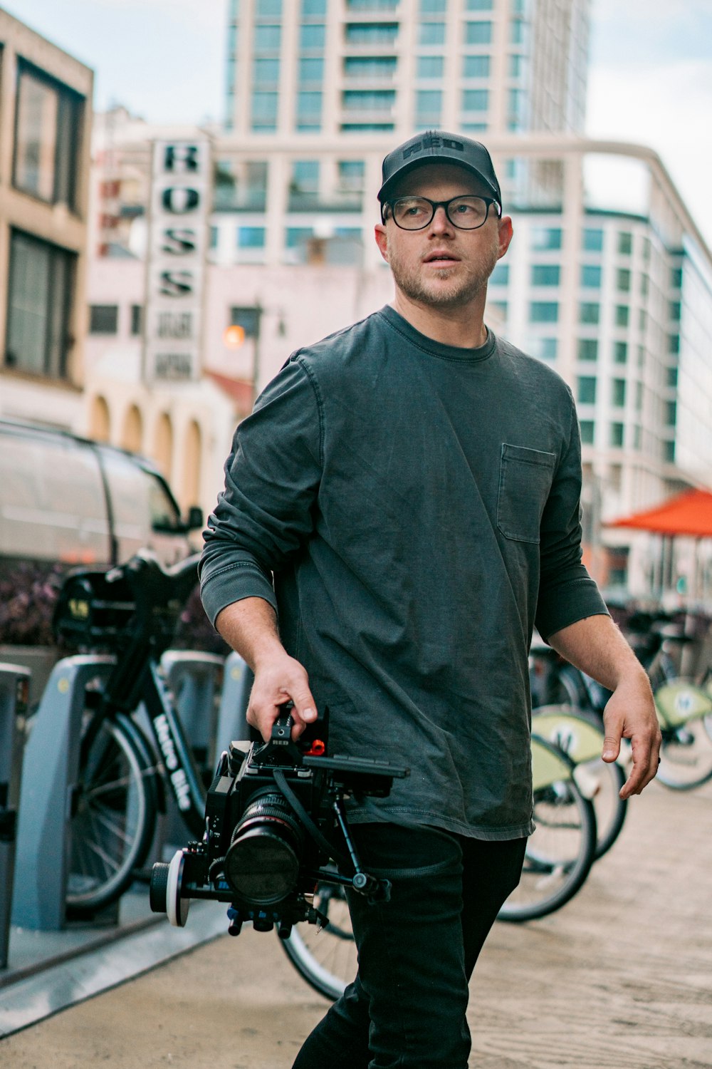 Mann in schwarzem Langarmhemd und schwarzer Sonnenbrille steht tagsüber neben einem schwarzen Fahrrad